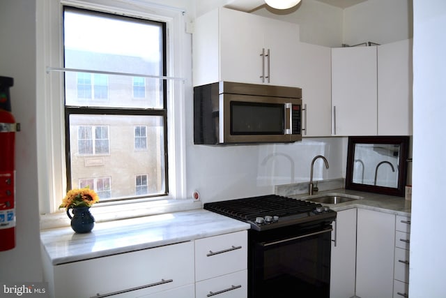 kitchen with black range with gas stovetop, white cabinetry, and sink