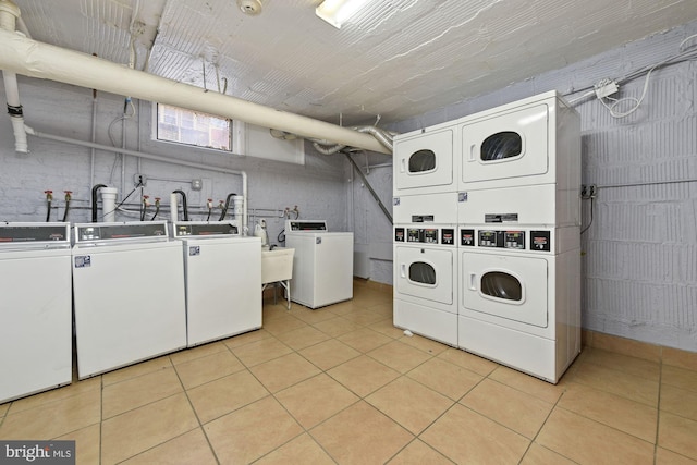 clothes washing area featuring stacked washer / drying machine, light tile patterned flooring, and washing machine and clothes dryer