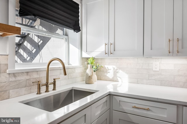 kitchen with tasteful backsplash, light stone countertops, and sink