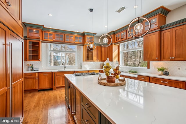 kitchen featuring light stone countertops, sink, hanging light fixtures, decorative backsplash, and light wood-type flooring