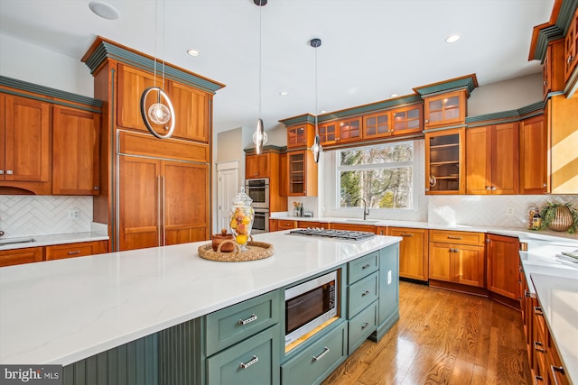 kitchen featuring sink, light hardwood / wood-style flooring, built in appliances, pendant lighting, and decorative backsplash