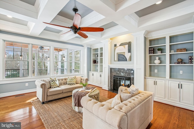 living room with built in shelves, ceiling fan, a premium fireplace, light hardwood / wood-style flooring, and decorative columns