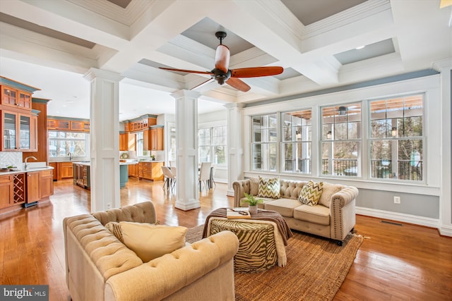 living room with decorative columns, ceiling fan, crown molding, light hardwood / wood-style flooring, and beamed ceiling