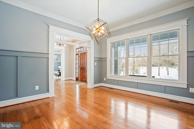 unfurnished dining area with ornamental molding, a chandelier, and light hardwood / wood-style floors