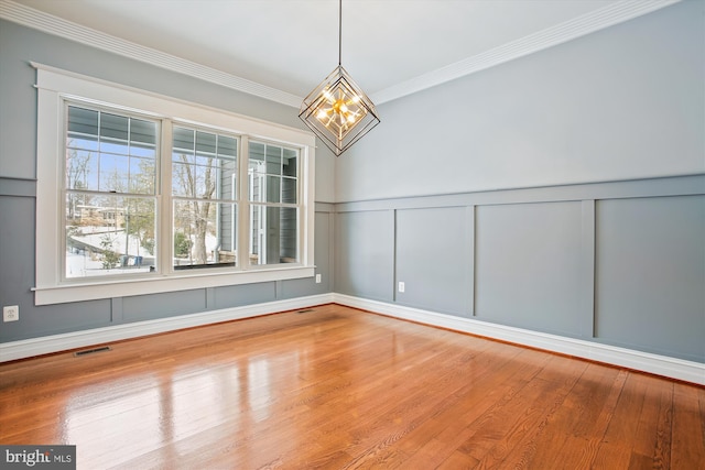 empty room featuring hardwood / wood-style flooring, crown molding, and an inviting chandelier