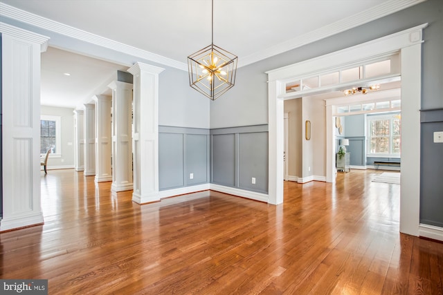 unfurnished dining area with decorative columns, crown molding, hardwood / wood-style floors, and a notable chandelier