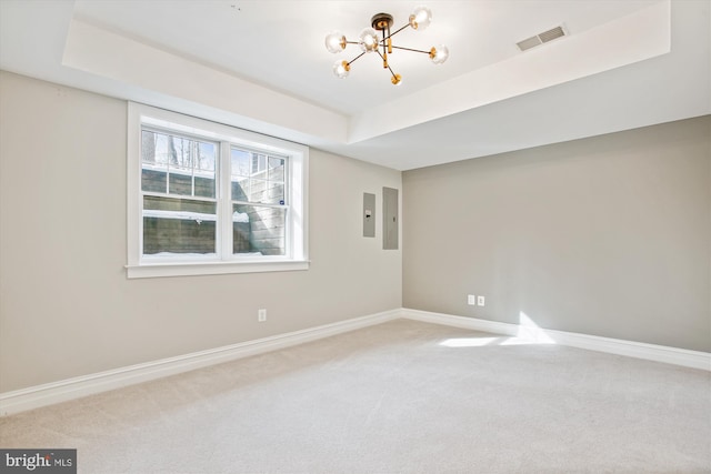 empty room featuring electric panel, an inviting chandelier, a raised ceiling, and light colored carpet