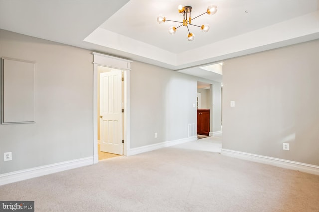 carpeted spare room with a tray ceiling and an inviting chandelier