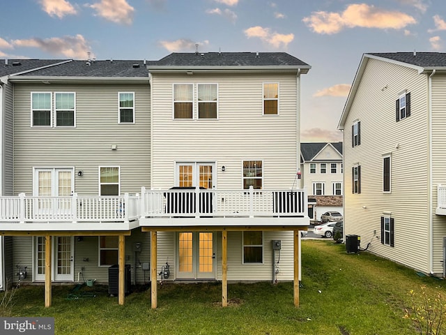 back house at dusk featuring a yard, a wooden deck, and central air condition unit