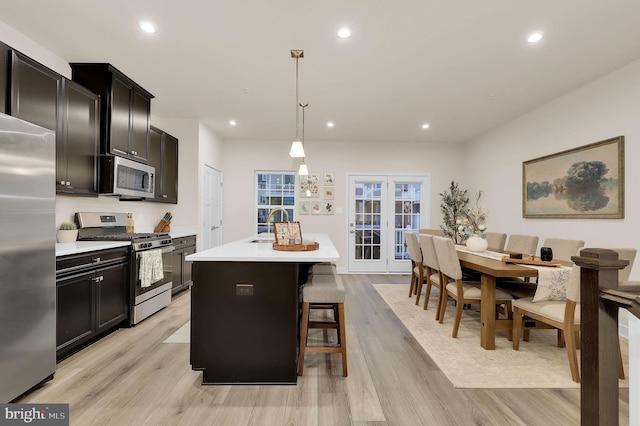 kitchen with stainless steel appliances, light hardwood / wood-style flooring, an island with sink, pendant lighting, and a kitchen bar