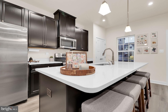 kitchen with appliances with stainless steel finishes, sink, pendant lighting, a center island with sink, and light hardwood / wood-style flooring