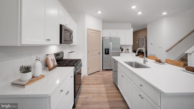 kitchen featuring appliances with stainless steel finishes, sink, light hardwood / wood-style flooring, white cabinetry, and an island with sink