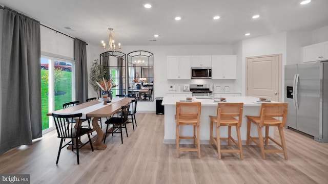 kitchen featuring white cabinetry, stainless steel appliances, an inviting chandelier, light hardwood / wood-style flooring, and a kitchen island with sink