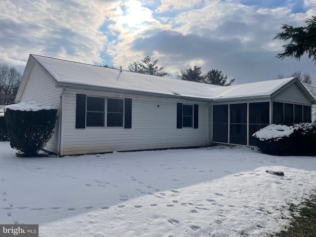 snow covered back of property featuring a sunroom