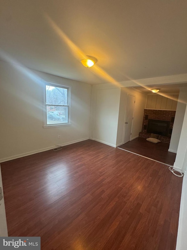 unfurnished living room with dark hardwood / wood-style flooring and a brick fireplace