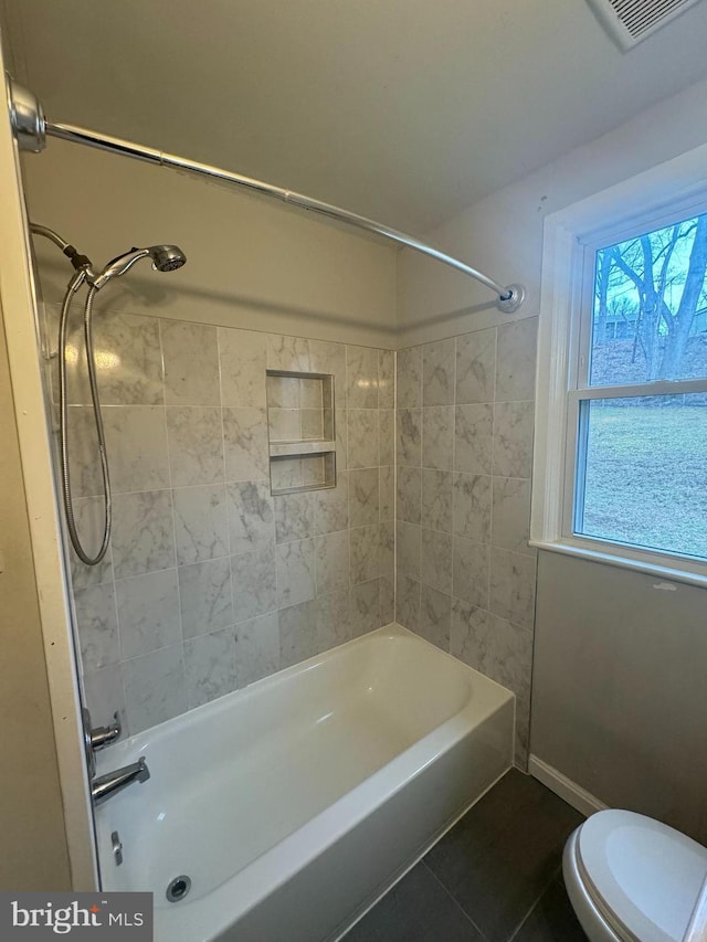 bathroom with tiled shower / bath combo, tile patterned floors, and toilet