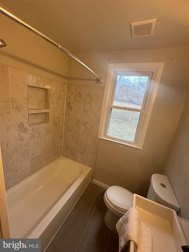 bathroom featuring tile patterned flooring, tiled shower / bath combo, and toilet