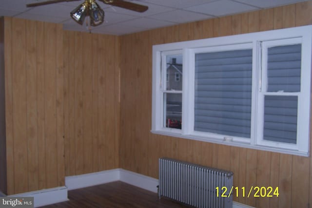 unfurnished room with a paneled ceiling, radiator, wooden walls, built in shelves, and dark hardwood / wood-style floors