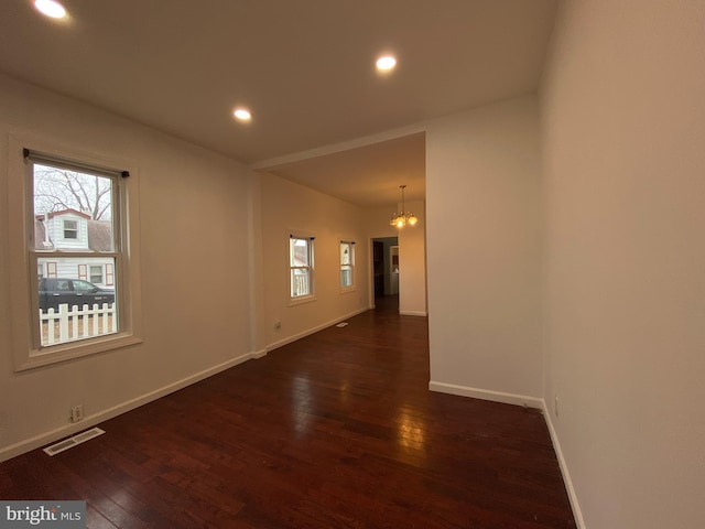 spare room featuring an inviting chandelier and dark wood-type flooring