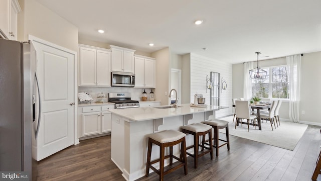 kitchen featuring a kitchen island with sink, sink, appliances with stainless steel finishes, decorative light fixtures, and white cabinetry