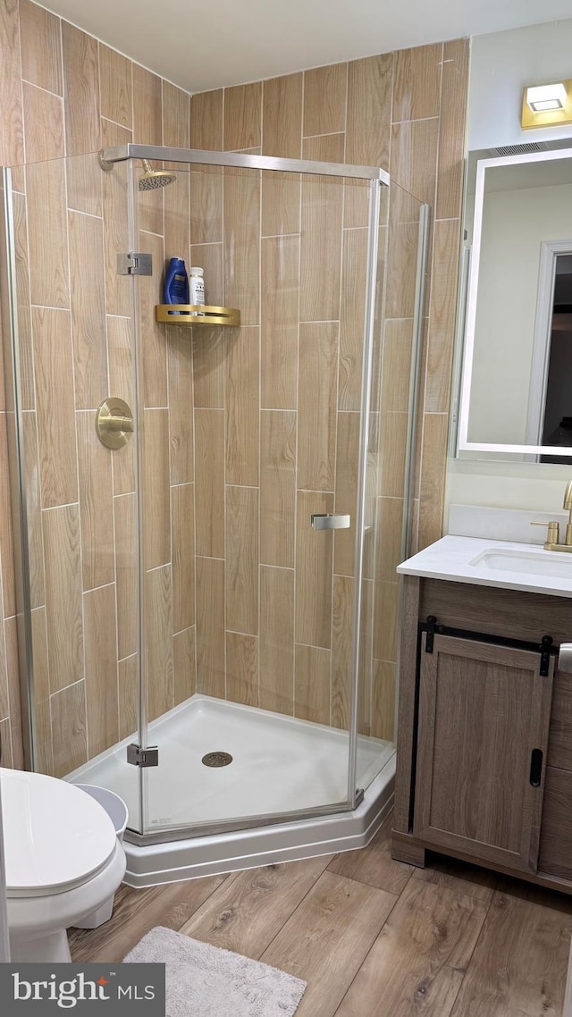 bathroom featuring a shower with door, vanity, hardwood / wood-style floors, and toilet