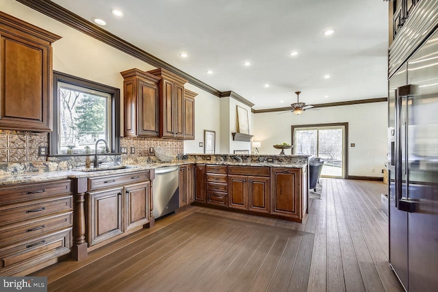 kitchen with kitchen peninsula, sink, stainless steel appliances, dark hardwood / wood-style flooring, and light stone counters