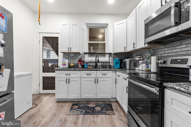 kitchen with sink, light hardwood / wood-style flooring, decorative backsplash, white cabinetry, and stainless steel appliances