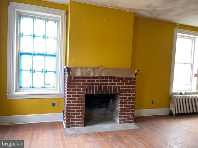 unfurnished living room featuring plenty of natural light, wood-type flooring, radiator, and a brick fireplace