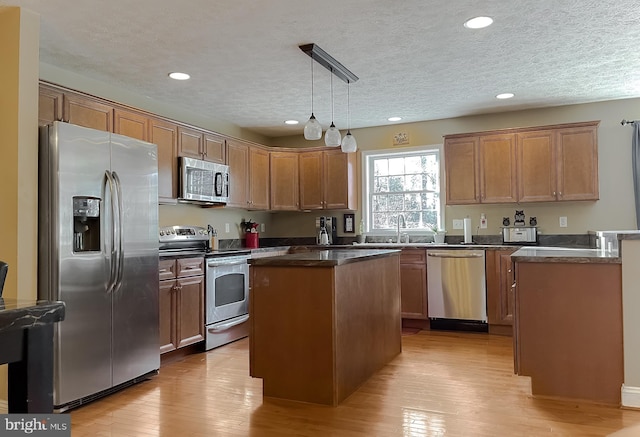 kitchen with a textured ceiling, stainless steel appliances, light hardwood / wood-style floors, a kitchen island, and hanging light fixtures