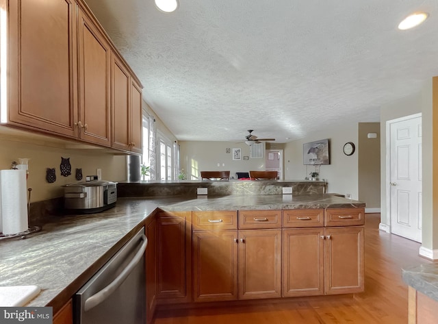 kitchen with ceiling fan, light hardwood / wood-style flooring, stainless steel dishwasher, kitchen peninsula, and a textured ceiling