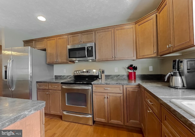 kitchen featuring a textured ceiling, sink, stainless steel appliances, and light hardwood / wood-style flooring