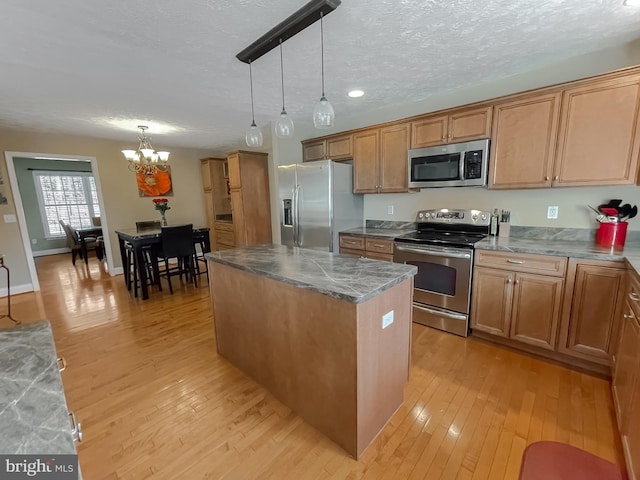 kitchen with light hardwood / wood-style flooring, a chandelier, decorative light fixtures, a kitchen island, and appliances with stainless steel finishes