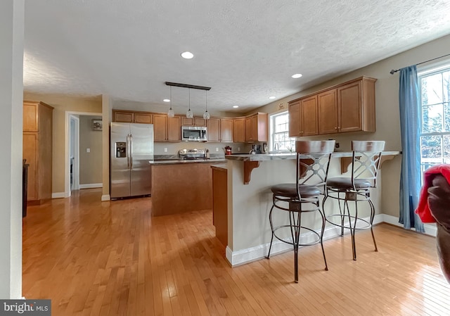 kitchen featuring pendant lighting, light wood-type flooring, a textured ceiling, a kitchen bar, and stainless steel appliances