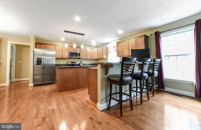 kitchen with appliances with stainless steel finishes, light wood-type flooring, decorative light fixtures, and a breakfast bar area