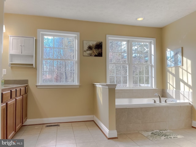 bathroom with tile patterned flooring, vanity, and a relaxing tiled tub