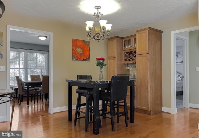 dining space with a textured ceiling, an inviting chandelier, and light hardwood / wood-style flooring