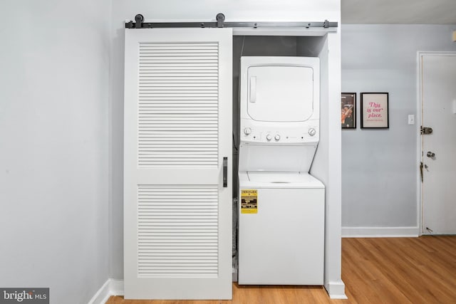 laundry room featuring a barn door, stacked washing maching and dryer, and light wood-type flooring