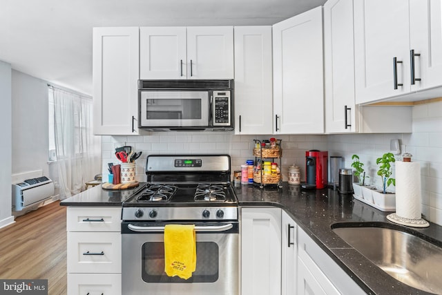 kitchen with dark stone counters, white cabinetry, stainless steel appliances, and light wood-type flooring