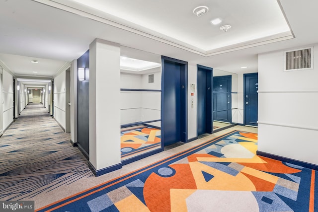 hallway featuring a raised ceiling, elevator, and carpet floors