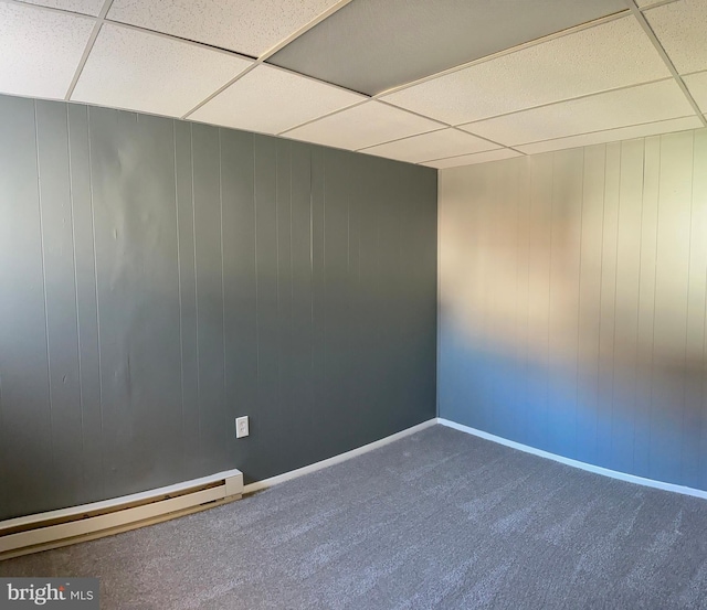 carpeted spare room with a baseboard radiator, a drop ceiling, and wood walls