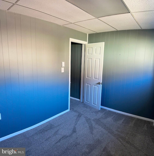 carpeted spare room with a drop ceiling and wood walls