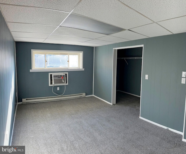 unfurnished bedroom with a drop ceiling, a baseboard radiator, a wall mounted AC, a closet, and carpet