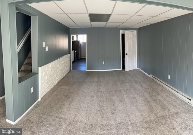 carpeted empty room featuring a drop ceiling and a baseboard heating unit