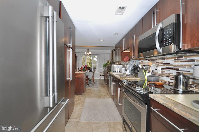 kitchen with appliances with stainless steel finishes, tasteful backsplash, ornamental molding, an inviting chandelier, and hanging light fixtures