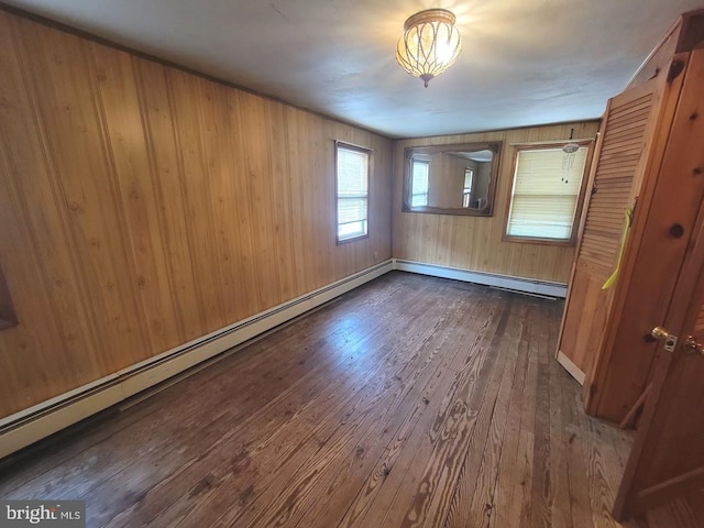 unfurnished room featuring wood walls, baseboard heating, and dark wood-type flooring