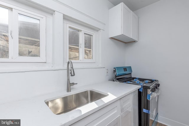 kitchen featuring white cabinets, sink, light stone countertops, and stainless steel gas range