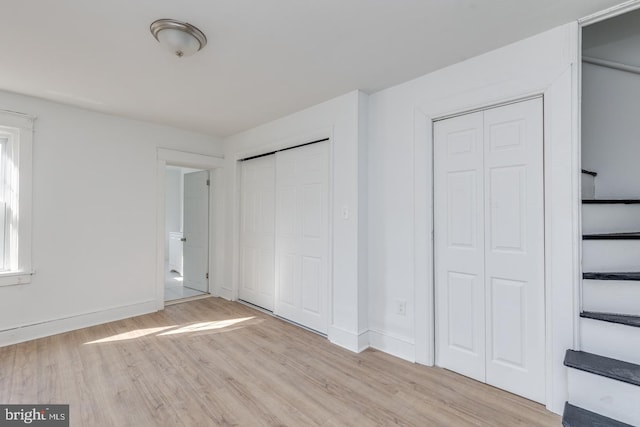 unfurnished bedroom with two closets and light wood-type flooring