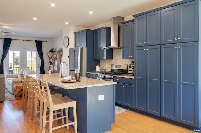 kitchen featuring a kitchen island with sink, wall chimney range hood, light hardwood / wood-style flooring, a kitchen bar, and stainless steel appliances