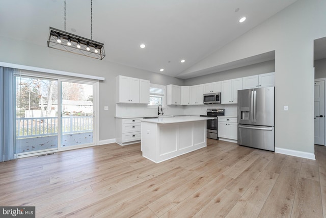 kitchen with light hardwood / wood-style flooring, appliances with stainless steel finishes, decorative light fixtures, a kitchen island, and white cabinetry