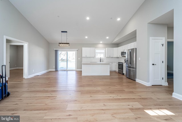 kitchen featuring white cabinets, light hardwood / wood-style floors, decorative light fixtures, a kitchen island, and appliances with stainless steel finishes